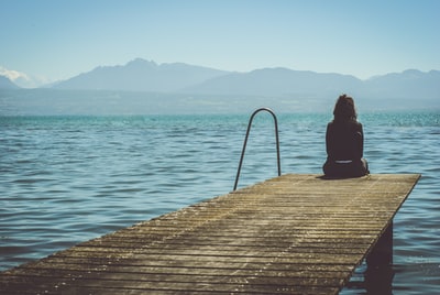 白天，一个女人坐在码头的尽头，凝视着湖面